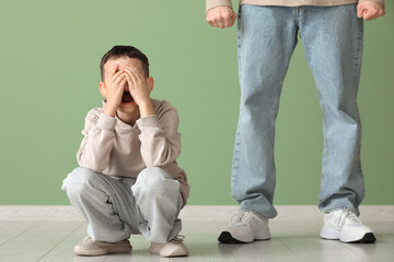 Crying boy with his father after squabbling near green wall