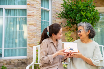 Happy Asian family adult daughter give present gift box to senior mother at home. Elderly mother celebration birthday party or mother's day with daughter in the garden. Family relationship concept.