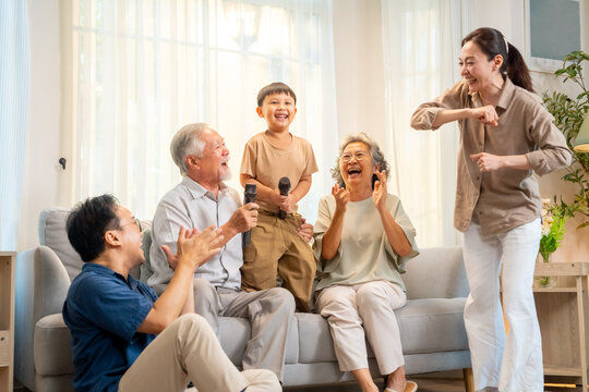 Happy Asian three generation family have fun singing and dancing together in living room. Big family grandparent and grandchild enjoy weekend activities lifestyle relaxing and playing together at home