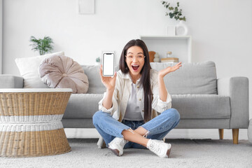 Obraz premium Excited young woman holding smartphone with blank screen, online shopping and mobile app promotion, home interior