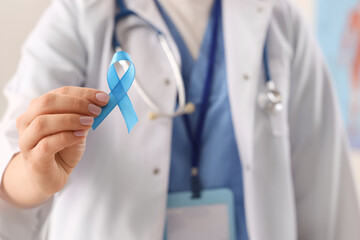 Female doctor with blue ribbon in clinic, closeup. Cancer awareness concept