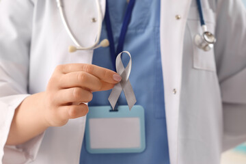 Female doctor with grey ribbon in clinic, closeup. Cancer awareness concept