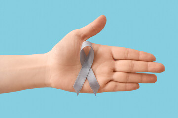 Female hand with grey ribbon on blue background. Cancer awareness concept