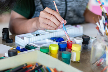 Drawing and coloring pictures of boys in art lesson at school by using poster colors and...