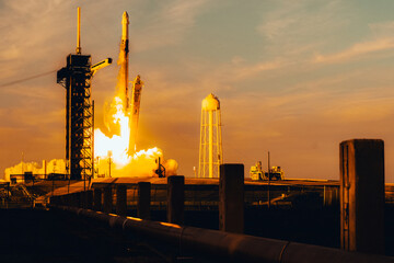 Rocket launch at sunset with fiery glow from launchpad, silhouetted against orange sky. SpaceX Falcon rocket blasting off. Technology and space concept. Elements of this image furnished by NASA