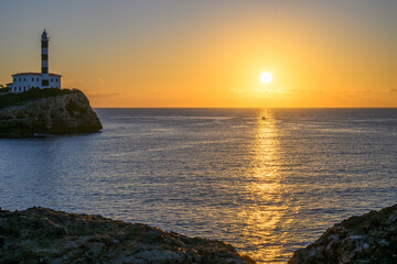 The lighthouse of Portocolomn on the island of Majorca with fishing boat in the light of the sunrise