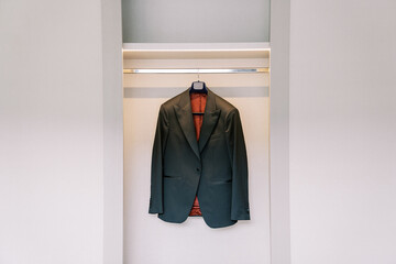 Groom black jacket hangs on a hanger in a white sliding wardrobe in the room
