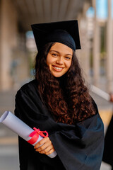 Young graduate smiling and holding her diploma, celebrating successful completion of studies on...