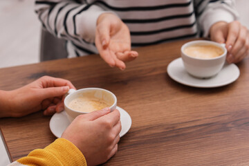 Coffee break. Women with cups of hot drinks at wooden table indoors, closeup