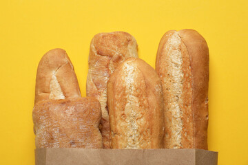 Paper bag with fresh baguettes and ciabatta on yellow background, top view