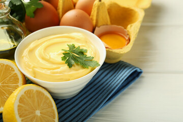 Delicious mayonnaise sauce with parsley in bowl and ingredients on white wooden table, closeup