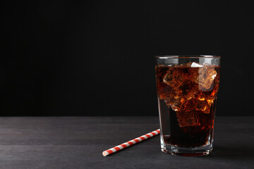 Refreshing cola with ice cubes in glass and drinking straw on black wooden table, closeup. Space for text