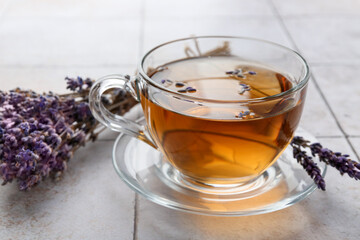 Aromatic lavender tea in glass cup and dry flowers on white tiled table, closeup