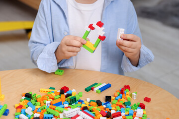 Fototapeta premium Cute boy playing with building blocks at wooden table indoors, closeup
