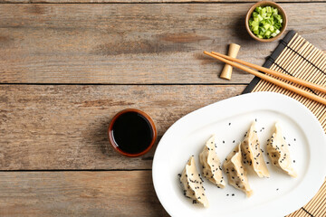 Delicious gyoza dumplings with sesame seeds served on wooden table, top view. Space for text