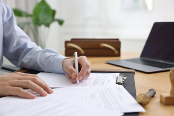 Notary signing document at table in office, closeup