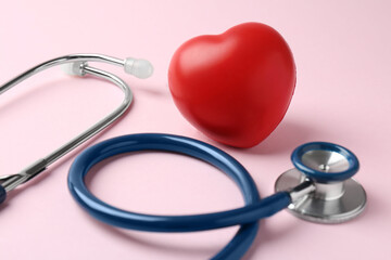 Cardiology. Stethoscope and red decorative heart on pale pink background, closeup