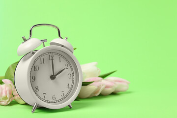 Spring time. Alarm clock and beautiful tulips on green background, space for text