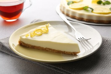 Piece of tasty lemon cheesecake and fork on grey textured table, closeup