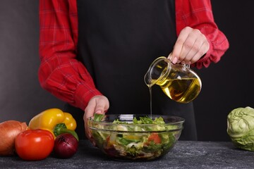 Woman pouring oil onto tasty salad at dark textured table, closeup