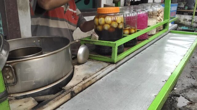 A man selling the traditional Javanese drink "Wedang Ronde" is putting the drink into plastic for takeaway service.