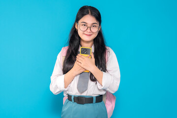 An Indonesian high school student in a school uniform with glasses and a backpack, holding her...