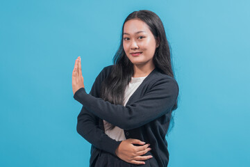 An Asian woman with long black hair wearing a black cardigan and white shirt stands against a blue...
