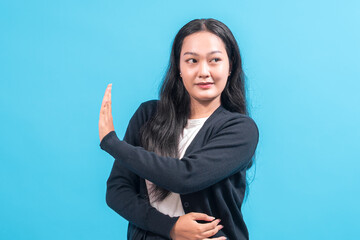 An Asian woman with long black hair wearing a black cardigan and white shirt stands against a blue...
