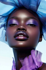 Fashion portrait featuring a young model adorned with striking purple makeup and a flowing blue and purple veil, presenting a bold, artistic aesthetic that captivates the viewer