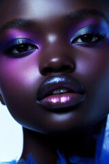 Close-up beauty portrait featuring a fashion model with vibrant, colorful makeup, showcasing bold purple eyeshadow and glossy lips, elegantly posed under soft blue lighting