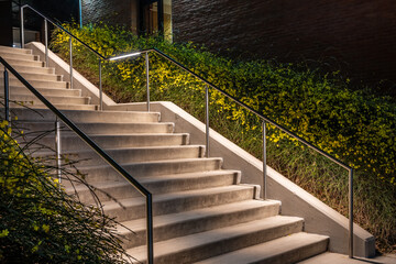Exterior night photo of a set of concrete stairs with stainless steel railing with integrated under...