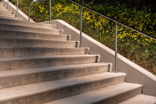 Exterior night photo of a set of concrete stairs with stainless steel railing with integrated under rail LED lighting.