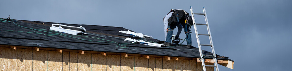 New home construction site, roofing contractor (workman labor) putting down asphalt shingles, housing development on a sunny winter day against a stormy sky  © knelson20