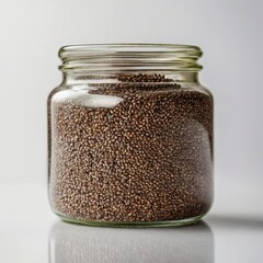 A jar of brown seeds sits on a white surface