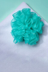 Bath essentials with an exfoliating sponge and a towel on an aqua green background, promoting self-care, skincare, and relaxation for a refreshing cleansing routine.