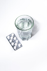 A glass of water and a blister pack of pills on a clean surface, representing medication, pharmaceutical treatment, healthcare, and medical prescriptions from pharmacies and laboratories.