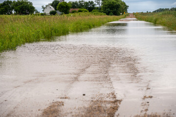 Selective focus on the gravel leading into floodwater covering the road in a rural area