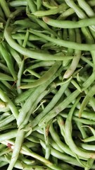A close-up image of freshly harvested green beans, also known as snap beans or string beans. The beans are long, slender, and vibrant green, with some showing natural imperfections such as brown spots