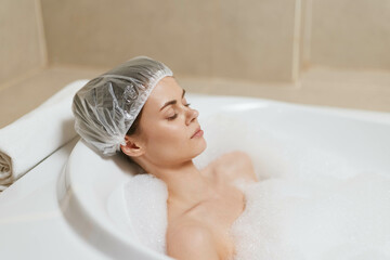 Relaxed young woman enjoying a soothing bubble bath, wearing a shower cap, immersed in tranquility,...