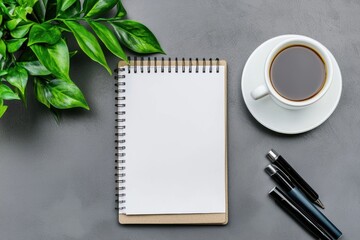 Modern workspace with green foliage spiral notebook coffee cup and pen set on gray surface background