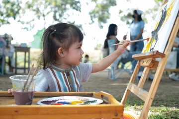 A young girl passionately painting on a canvas outdoors, surrounded by nature, showcasing...