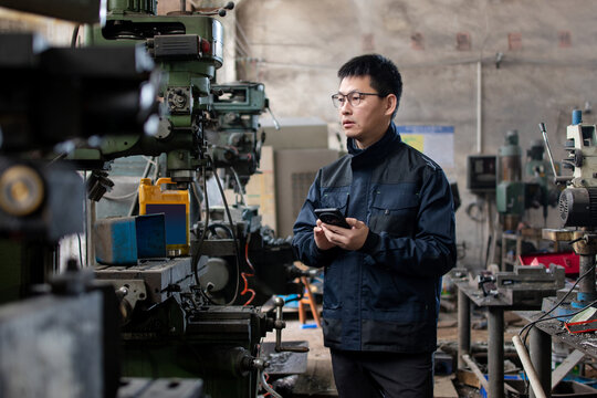 Asian male blue  collar workers are using smart phone in a metal processing factory