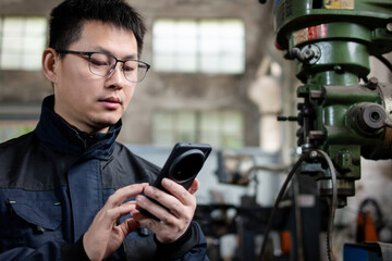 Asian male blue  collar workers are using smart phone in a metal processing factory
