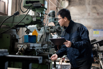 Asian male blue collar worker using digital tablets in a metal processing factory