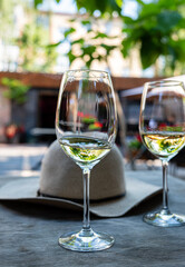 Two elegant glasses of white wine sit on a rustic table beside a chic hat in warm sunlight