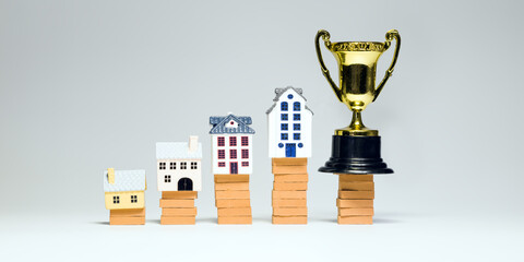 Miniature houses stacked on bricks with a trophy symbolize growth in real estate investments,...