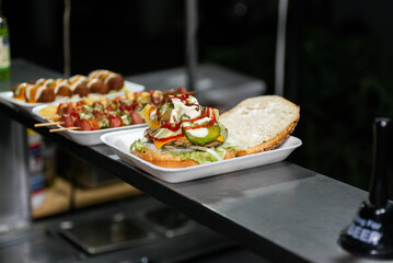 Close-up of a freshly prepared burger, garnished with various toppings, resting on a disposable...