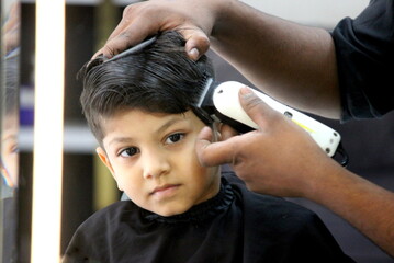 Boy is getting his haircut done at salon. Barber is cutting hair of a 4 year old cute little boy at...