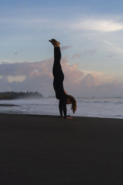 Woman practicing yoga at beach against clear sky during sunset