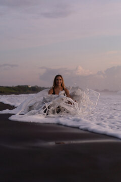 Beautiful woman in the foam of the waves on the beach at sunset. Bali